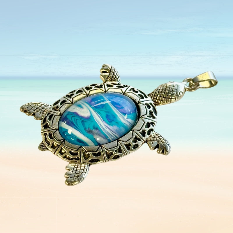Turtle-shaped pendant with a blue and white marbled stone on a beach background