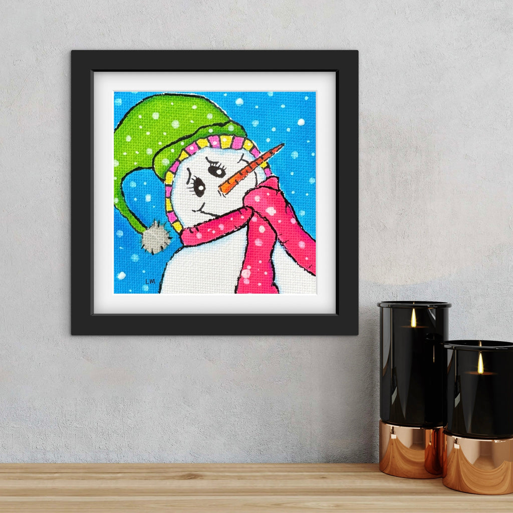 Framed artwork of a colorful snowman on a wall with decorative candles below.