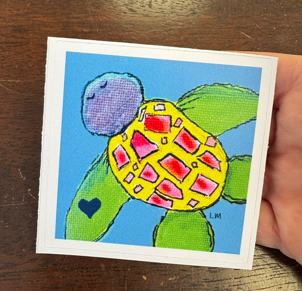 Colorful turtle sticker held by a hand on a wooden surface