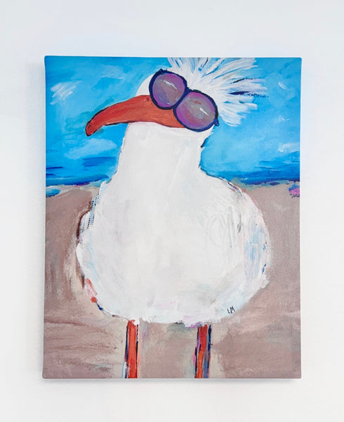 A rectangular canvas print of a white seagull with an orange beak, purple round sunglasses, and a white crest, standing on a sandy beach under a bright blue sky