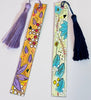 Two painted paper bookmarks with tassels, displayed on a plain white background. The left bookmark is yellow with purple, red, and white abstract floral patterns and a purple tassel.