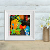 abstract art in a white frame against a wall next to a vase of flowers