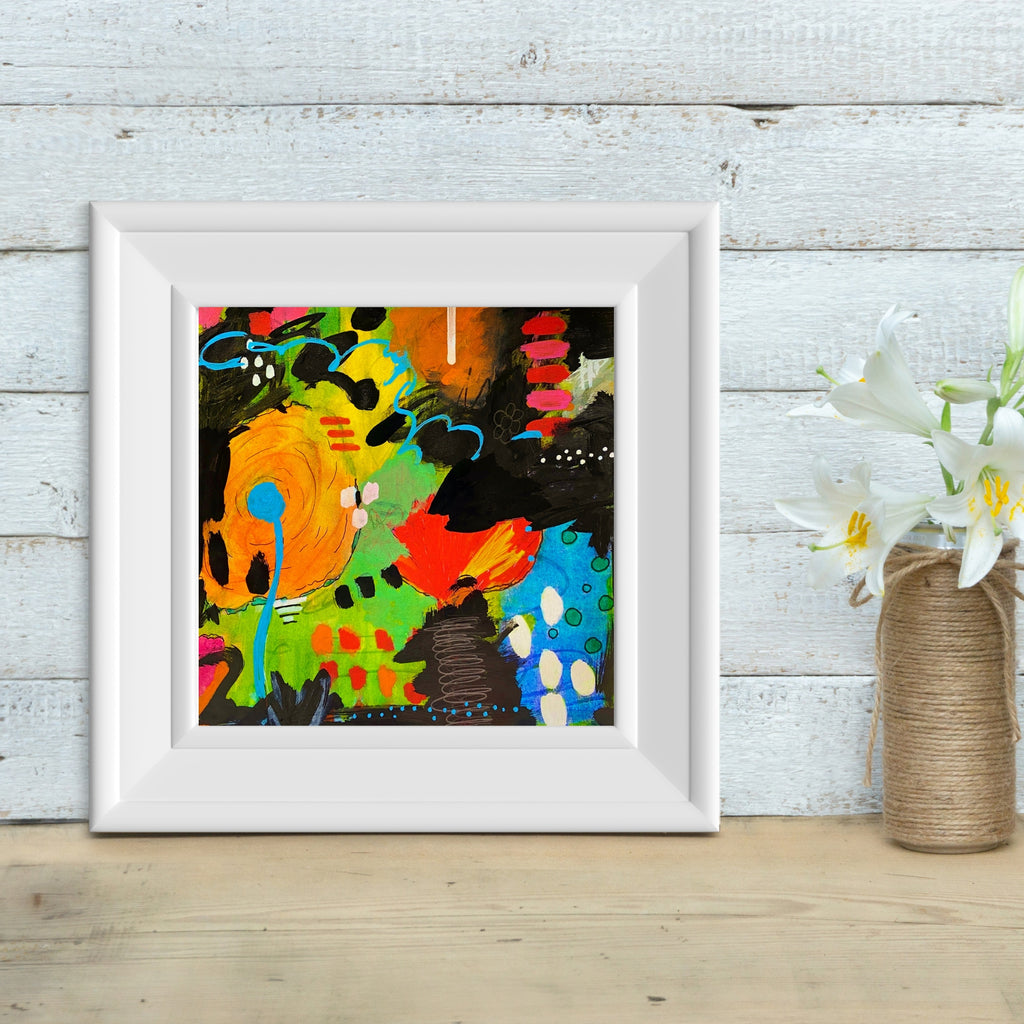 abstract art in a white frame against a wall next to a vase of flowers