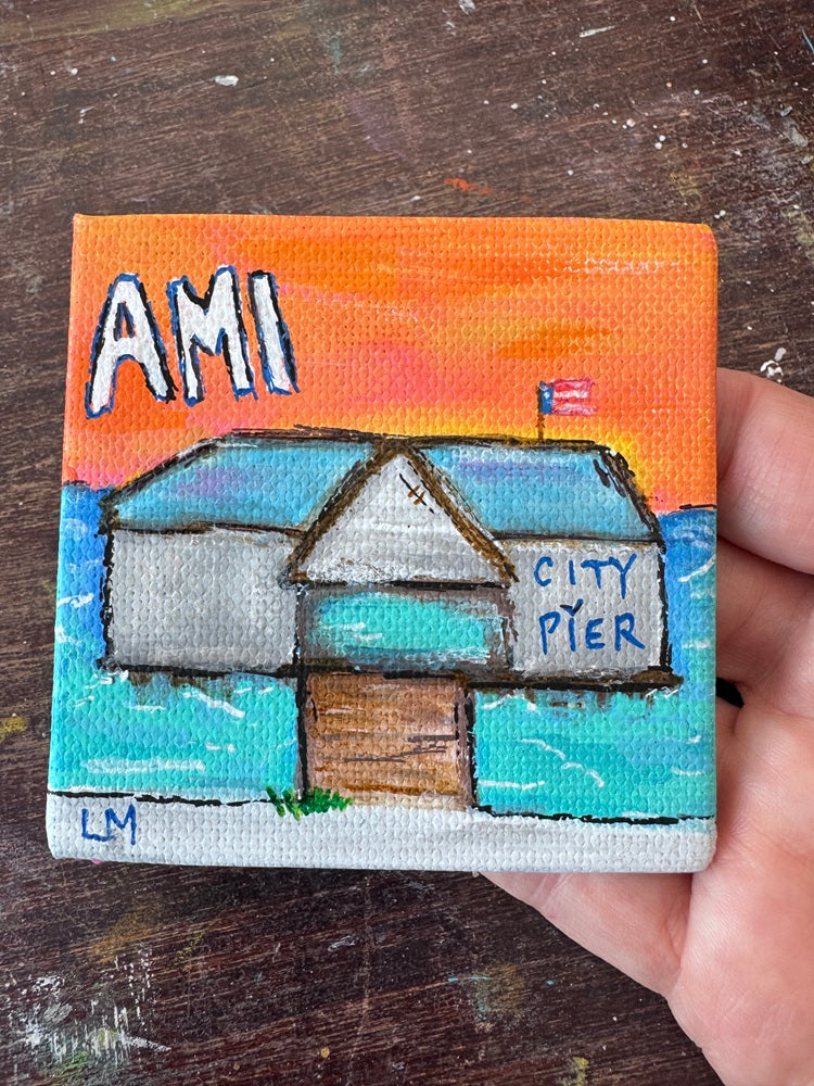 a small painting with text 'AMI City Pier' featuring a building on a pier over water with a sunset