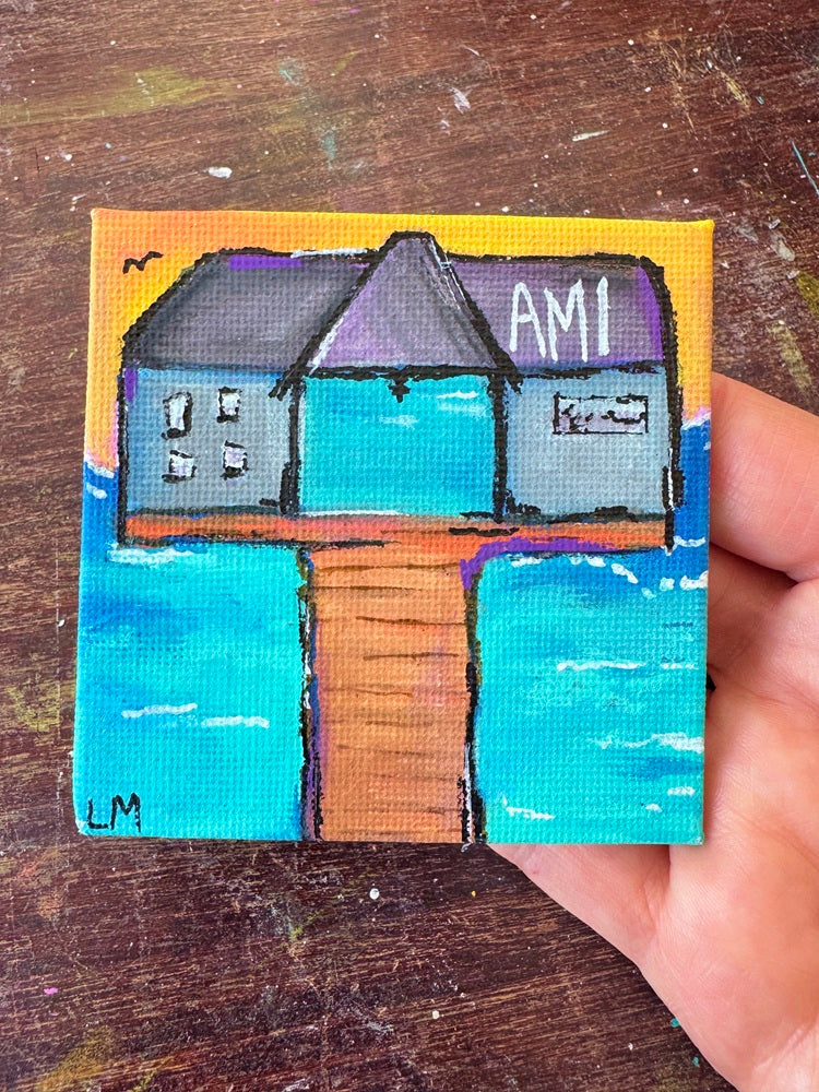 small painting with a pier and text 'AMI' with water and a sunset sky being held by a hand