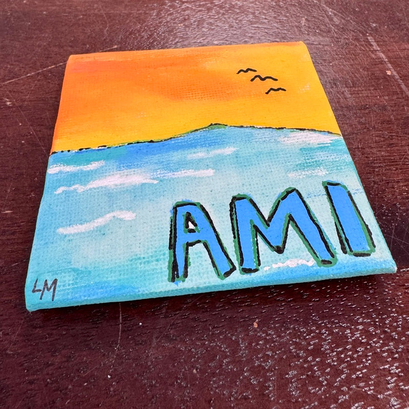 Small painted canvas with a sunset over water scene and 'AMI' text, pictured on a wooden surface.