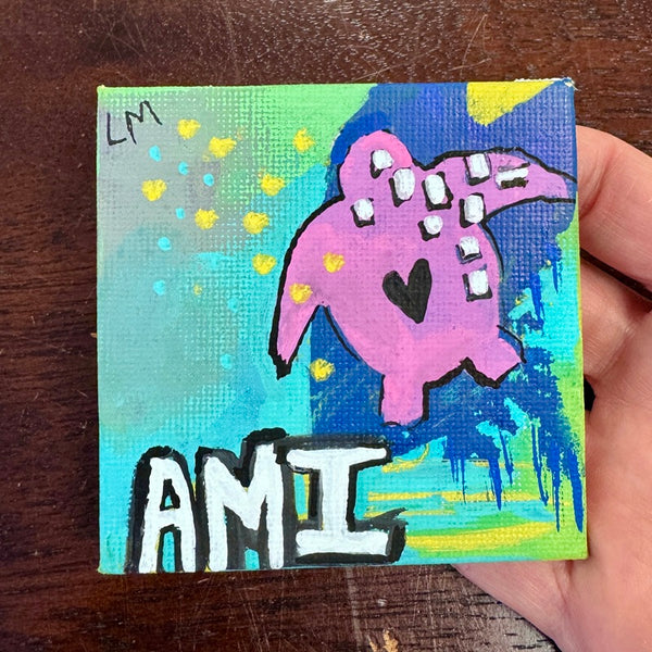 Small painted canvas with a pink turtle and 'AMI' text, held by a hand on a wooden surface.