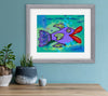 Framed colorful fish painting on a wall with plants and a small sculpture below.