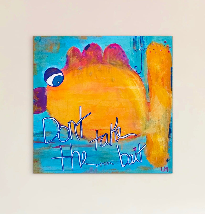 A square canvas painting featuring a whimsical orange and yellow fish with blue eyes on a turquoise background, with the handwritten text 'Don't take the bait' in blue. The canvas is mounted on a light beige wall.