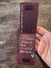 A long rectangular piece with scalloped edges, black rectangular magnets and handwritten white text on a worn wooden tabletop.