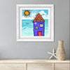 Framed artwork of a house by the sea on a gray wall with a vase and starfish below.