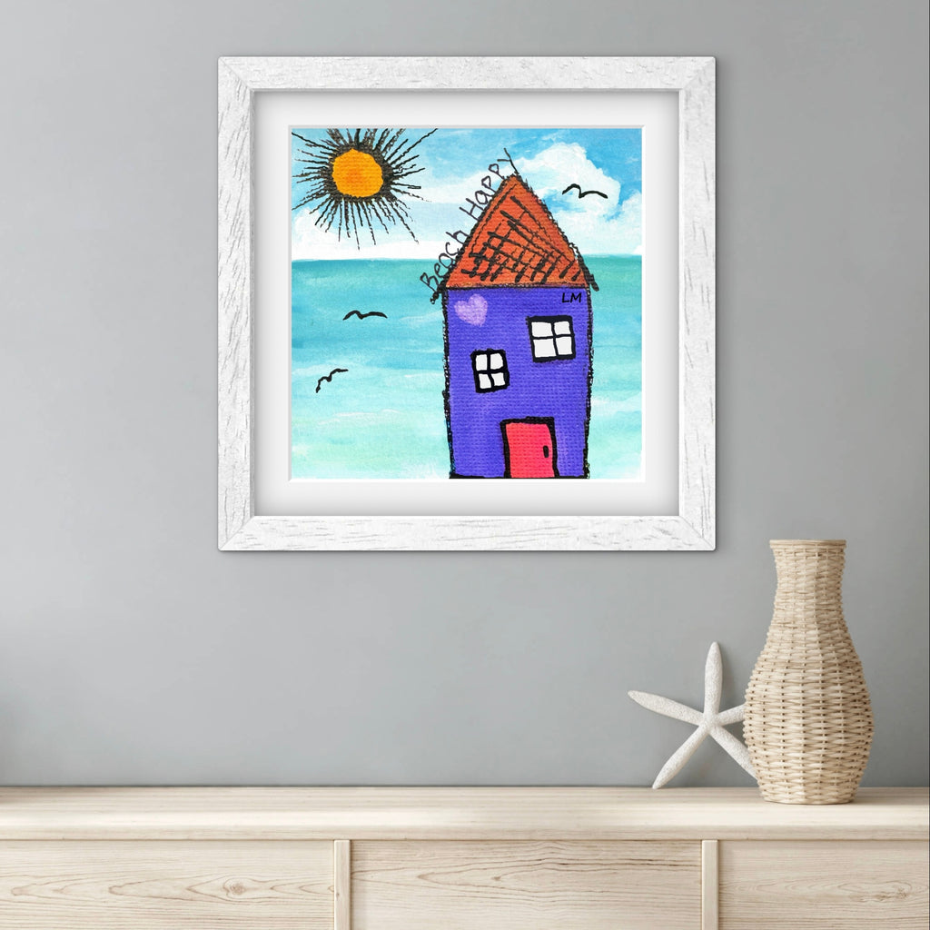 Framed artwork of a house by the sea on a gray wall with a vase and starfish below.