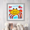 Framed artwork of a colorful crab with 'beach happy' text on a light gray wall.