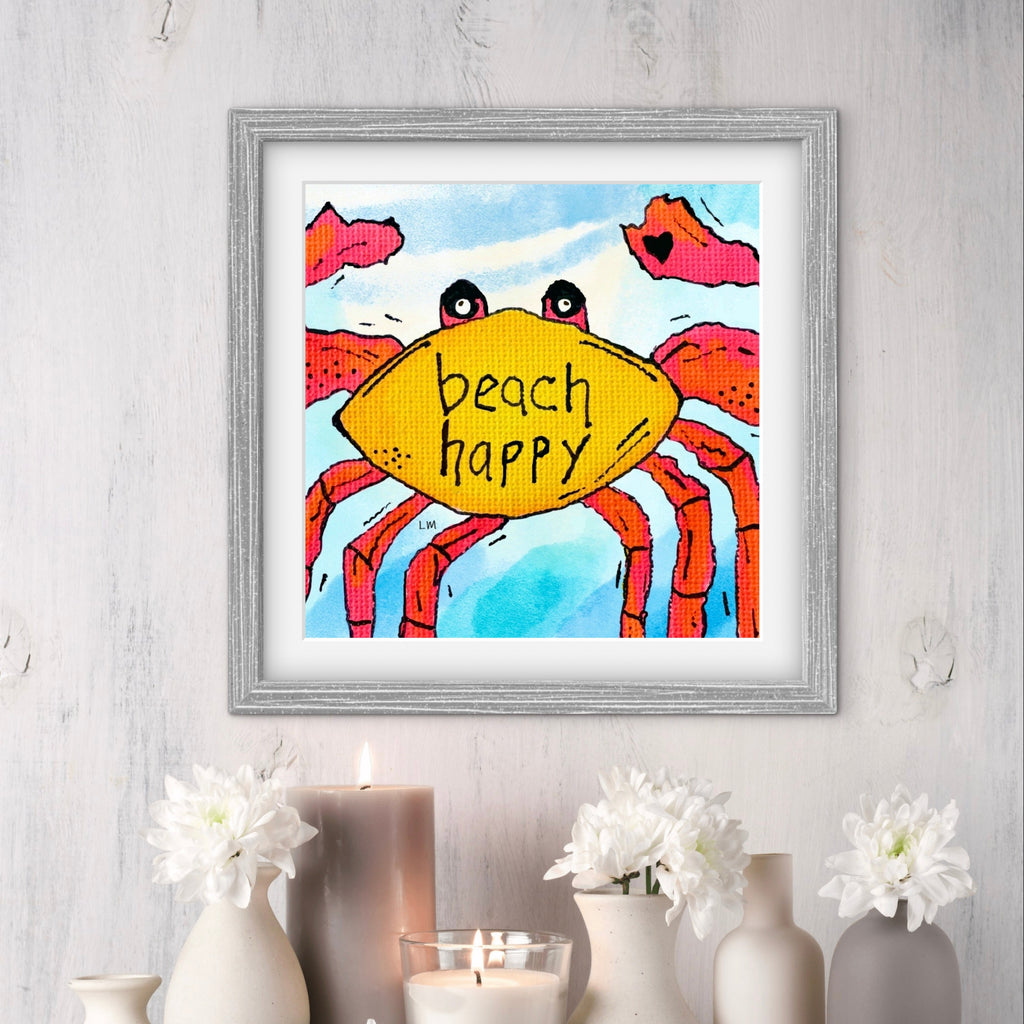 Framed artwork of a colorful crab with 'beach happy' text on a light gray wall.
