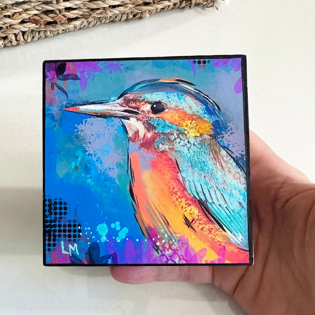 Birds of Color art block held in one hand for scale, showing a turquoise, orange, and pink bird on a blue background 