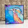 Birds of Color art block featuring a turquoise, orange, and pink bird on a blue background, displayed on a white surface against a woven basket.