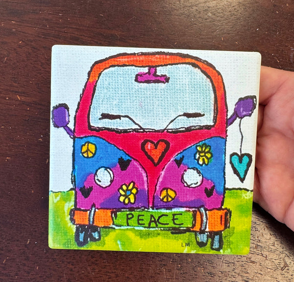 A square coaster with an image of a colorful, retro-style peace van being held by a hand over a dark wooden surface.