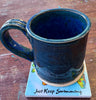 a coffee mug sitting on a square coaster that has text "Just Keep Swimming on a dark tabletop