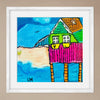 Colorful artwork of a house by the sea with a white frame on a beige wall.