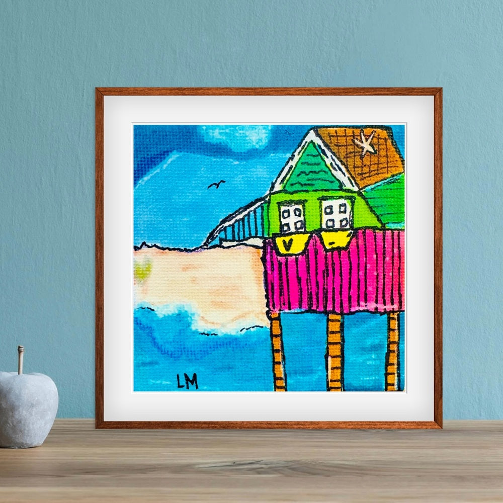 Framed colorful painting of a house on stilts against a blue wall.