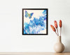 Expansion butterfly painting in a black frame on a white wall beside a cream vase with red-orange flowers