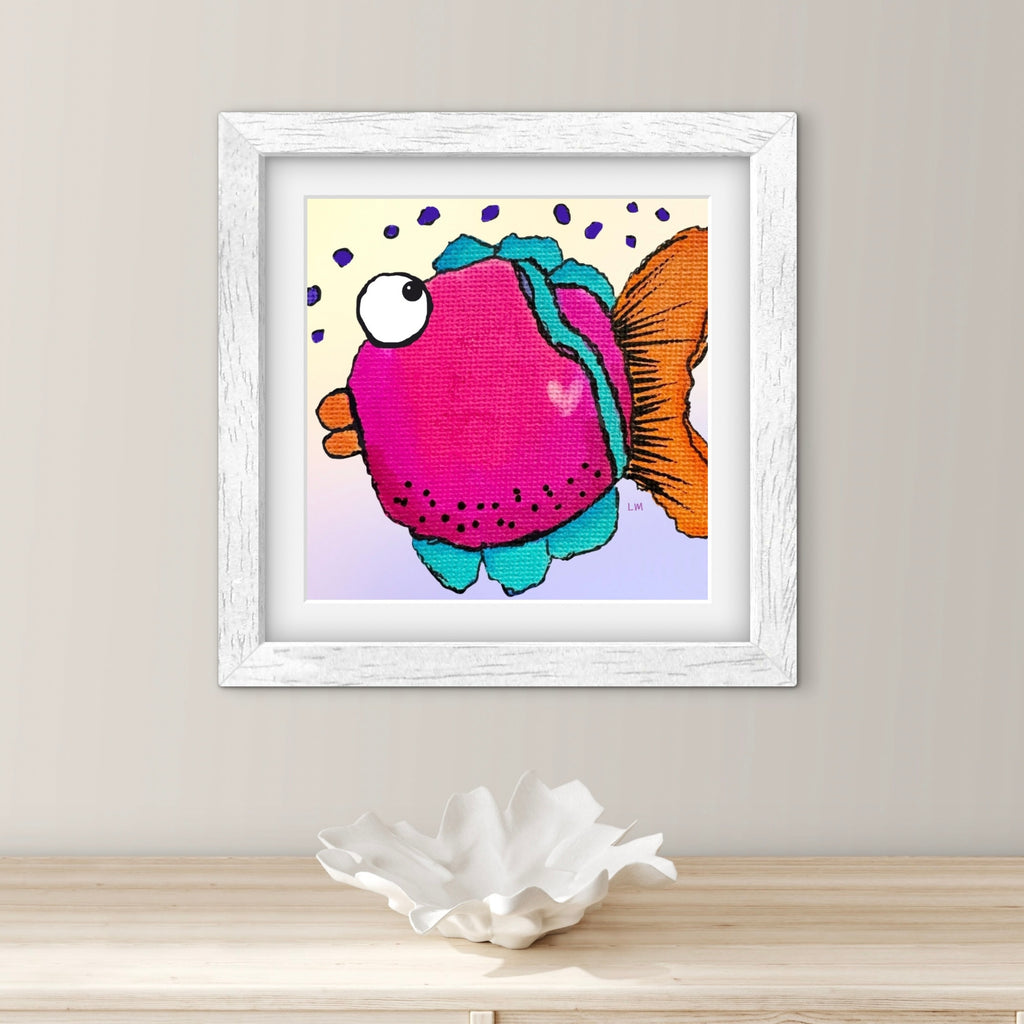 Framed artwork of a colorful fish on a wall above a wooden surface with a shell.