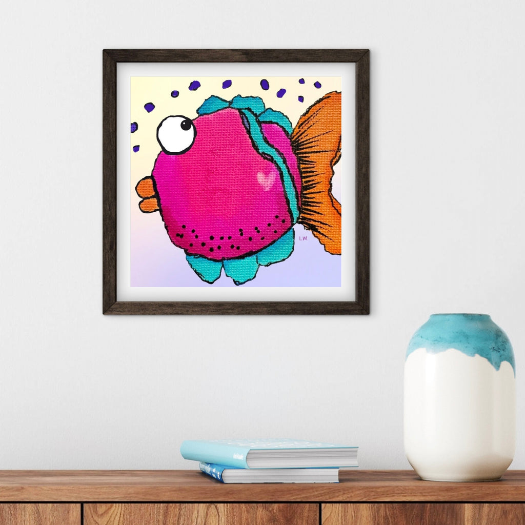 Framed artwork of a colorful fish on a wall above a wooden surface with a vase and books.