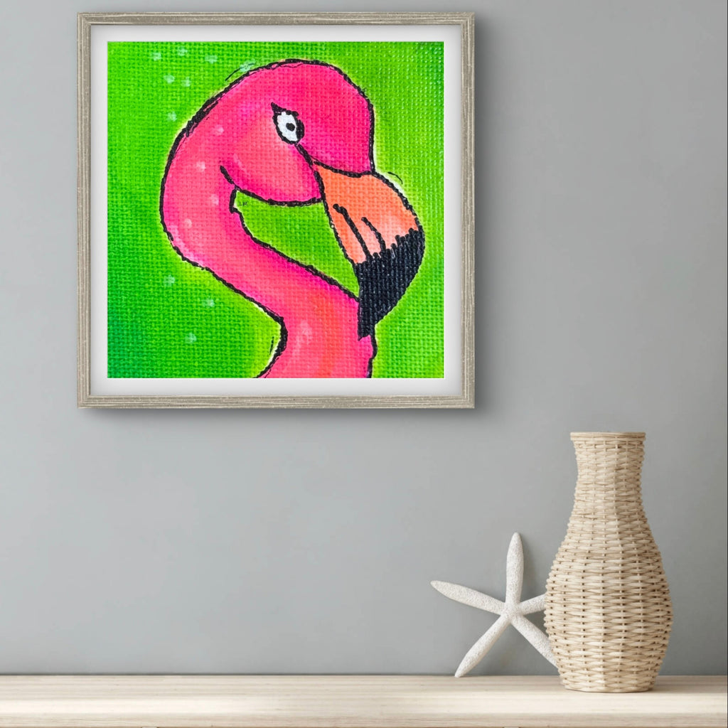 Framed artwork of a pink flamingo on a green background, displayed on a wall with a vase and starfish below.