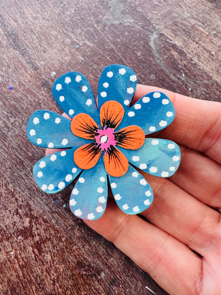 Hand holding a blue flower-shaped magnet with white polka dots on a wooden surface