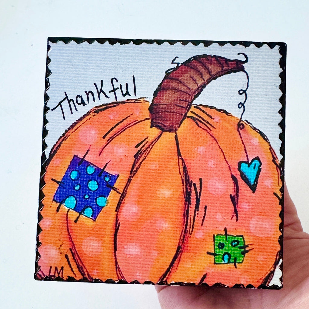 whimsical pumpkin painting on a wood block and the text 'thankful'