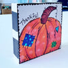 whimsical pumpkin painting on a wood block and the text 'thankful', The sides are painted with black and white stripes
