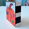 whimsical pumpkin artwork on a wood block and the text 'thankful', The sides are painted with black and white stripes