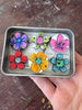 Colorful flower-shaped magnets in a metal box held by a hand on a wooden surface.