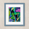 A framed abstract painting featuring vibrant green, blue, pink, and yellow brushstrokes, set in a slate blue frame with a white mat against a textured beige wall