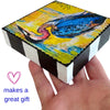 a hand holding a painting on a wood block with text next to it reading 'makes a great gift'