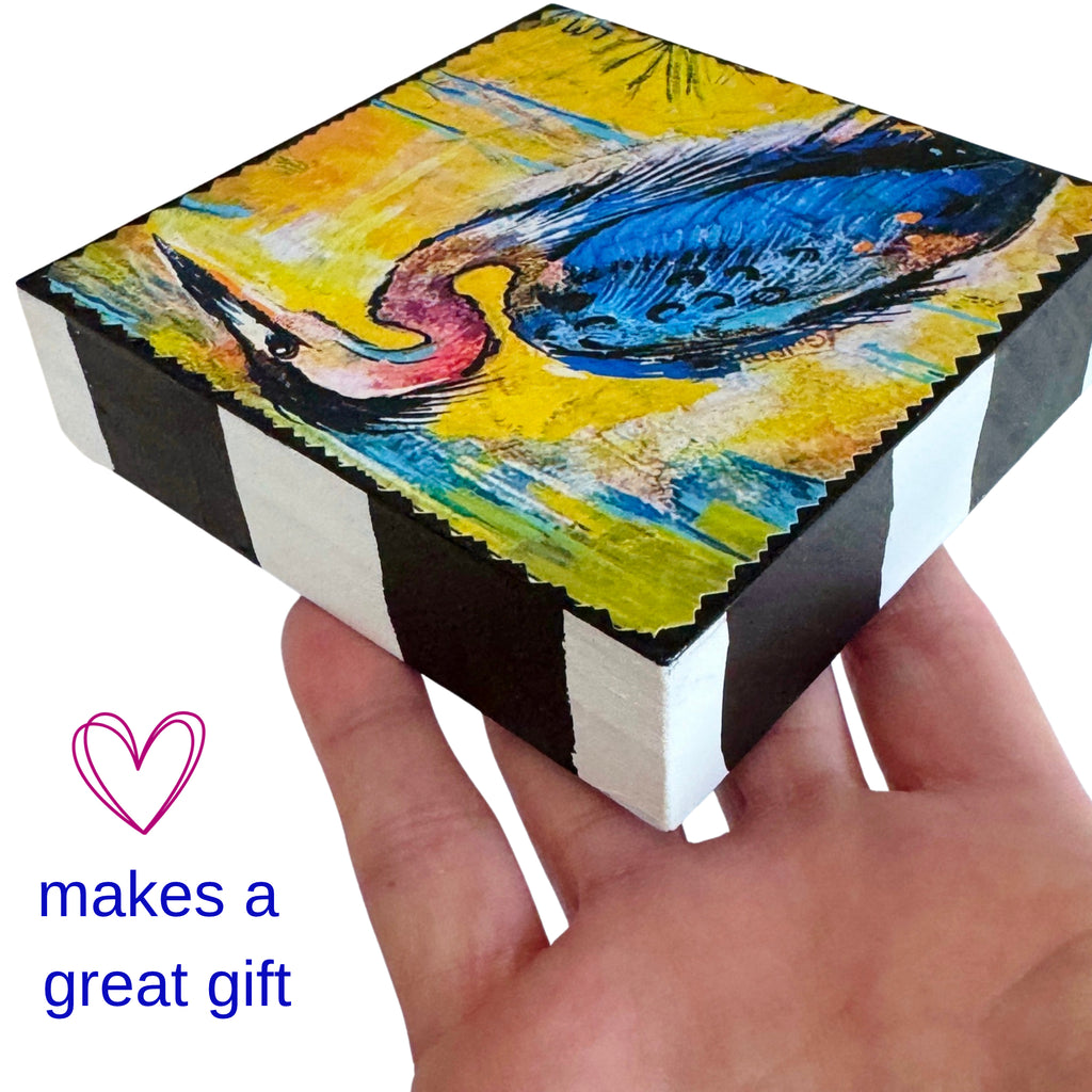 a hand holding a painting on a wood block with text next to it reading 'makes a great gift'