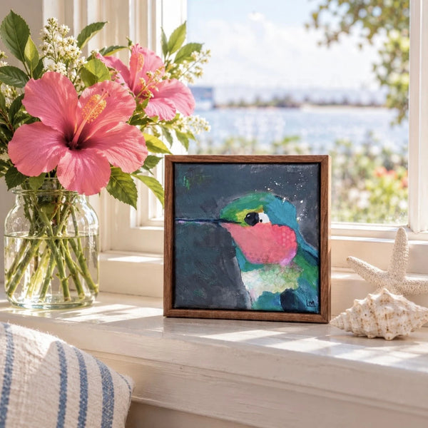 a framed painting in a windowsill next to a vase of flowers and seashells with water inlet in the background
