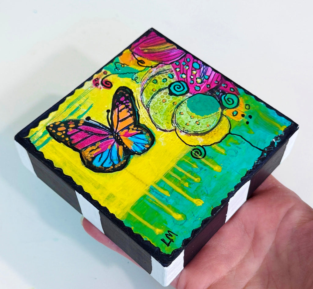a hand holding colorful artwork featuring a butterfly and abstract flowers