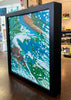 a colorful painting in a black frame on a table