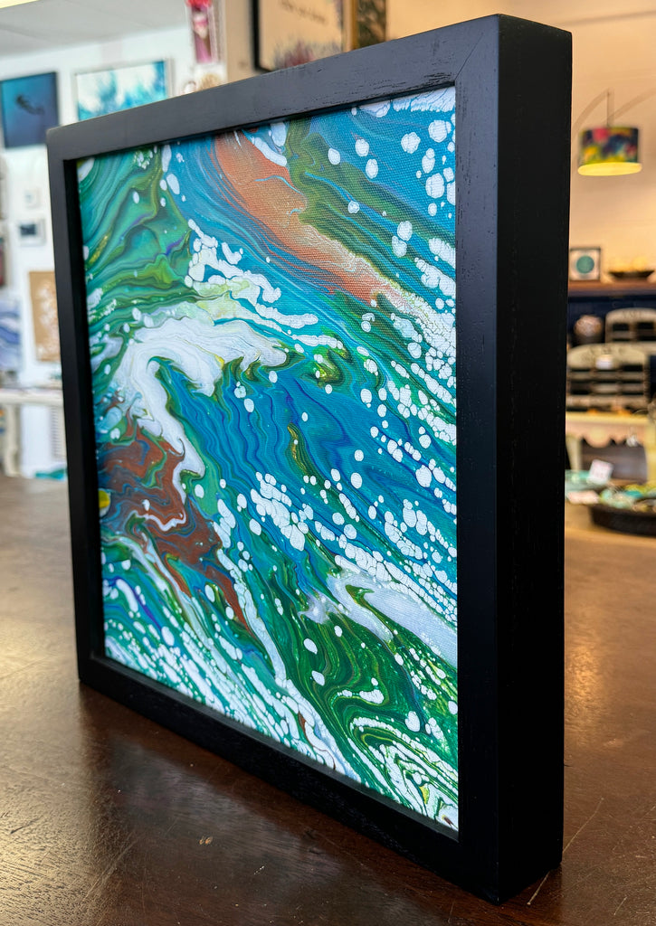 a colorful painting in a black frame on a table