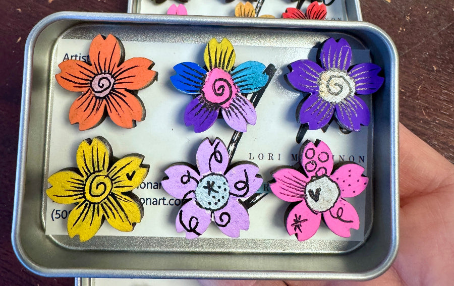 Colorful flower-shaped magnets in a metal case held by a hand.