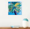 abstract style palm tree painting on a square canvas on a white wall above a table with a vase and books