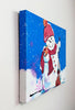 A canvas print featuring a whimsical painted snowman on a bright blue snowy background, hanging on a white textured wall.