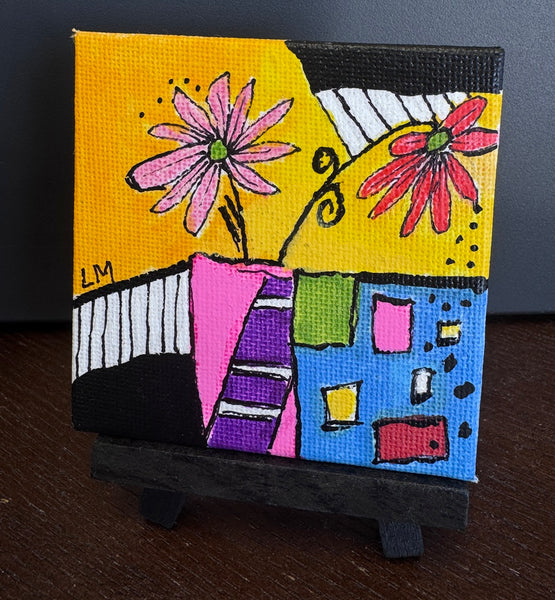 A small square canvas painting displayed on a black easel stand, featuring a colorful abstract floral design with pink flowers, a yellow background, black and white striped shapes, and blocks of blue, green, pink, purple, and red.