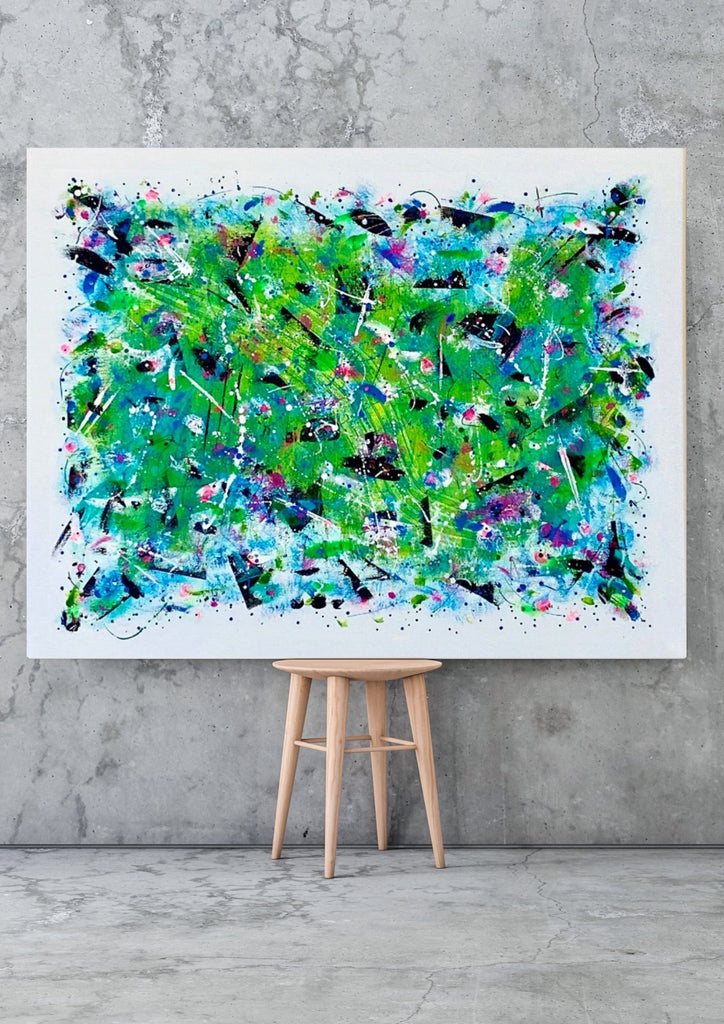 Abstract painting with vibrant colors on a white frame, leaning against a gray wall.