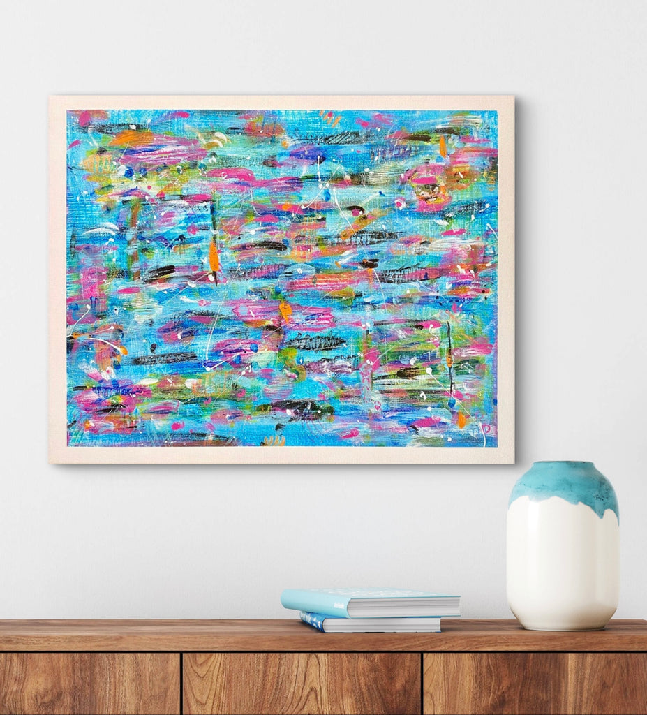 Framed abstract painting with colorful brush strokes on a white wall above a wooden shelf.