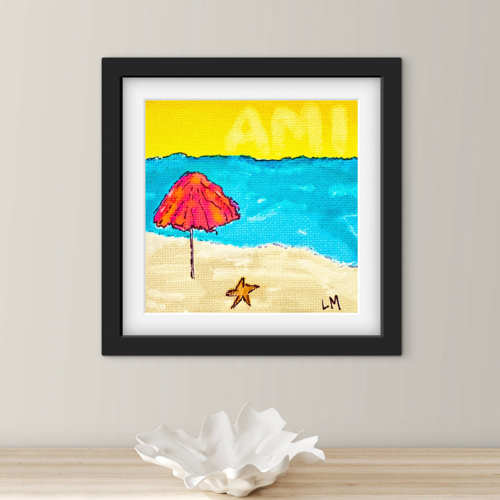 Framed artwork of a beach scene with a pink umbrella and blue sky on a light gray wall.