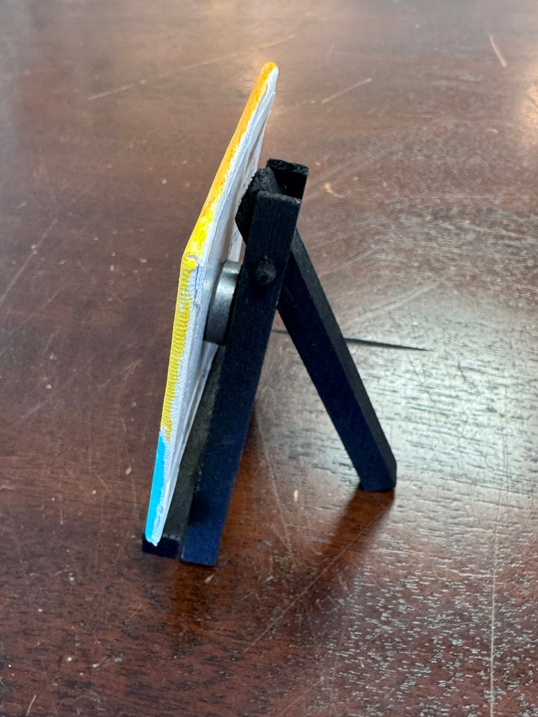Small black stand holding a yellow and blue object on a wooden surface