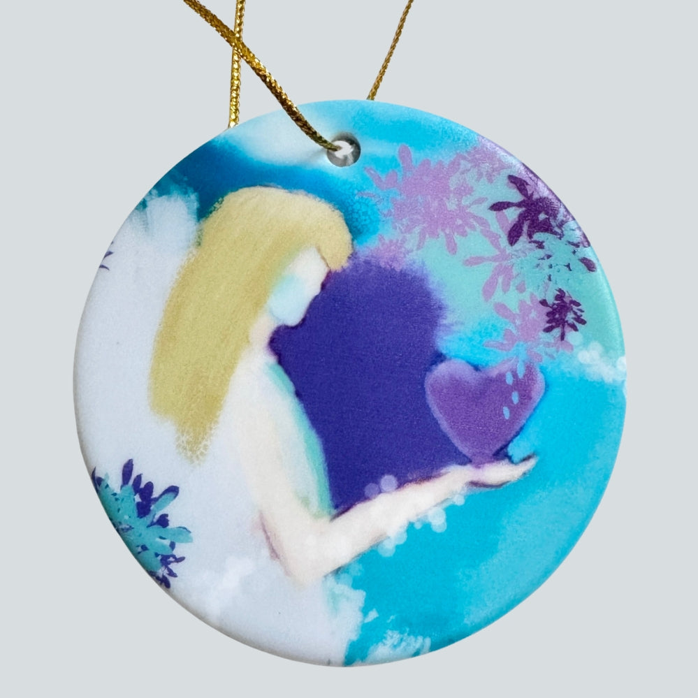 Round ceramic Christmas ornament featuring a angel with blonde hair holding a purple heart, set against a blue and white background with purple floral accents, hanging from a gold string.