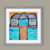 Framed artwork of a building on a pier with 'AMI' branding, set against a beach scene.